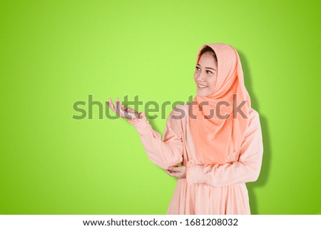 Pretty young muslim woman showing blank area for sign or copy space in the studio with green background