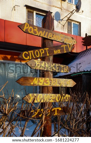 Wooden direction post with Russian inscriptions meaning TAP BEER, SPORTS AND TV, BANQUETS, MUSIC, COMFORT, COZINESS.