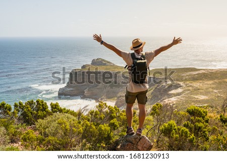 Wanderlust Traveler guy posing on stone at Cape of Good Hope, South Africa. Man in straw hat enjoying breathtaking landscape nature view on sea coast. Summer holiday vacation relax time at seaside. Royalty-Free Stock Photo #1681230913