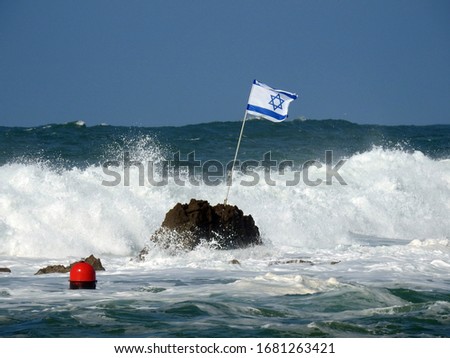 Israeli flag waving in the wind in the Mediterranean Sea with waves breaking on rock (Andromeda rock by Jaffa)