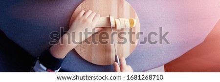 a 6 year old child cutting a ripe banana on grey background