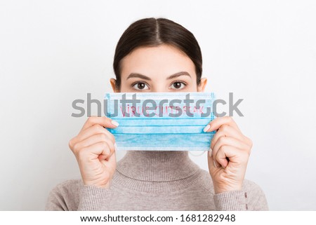 Portrait of pretty woman holding medical mask with virus outbreak text in hands at white background. Coronavirus concept. Respiratory protection.
