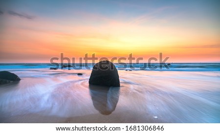 Dawn on beautiful beache with waves crashing on the shore creating silk-like streaks of different shapes piercing the rock.  Royalty-Free Stock Photo #1681306846