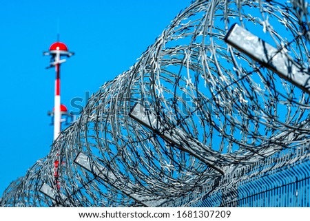 fence with barbed wire and row of the airport lamp posts with alternate red and white painting against blue sky, security concept