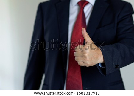 Successful businessman in suit and red tie shows thumbs up gesture. Thumb up is a symbol of approval.