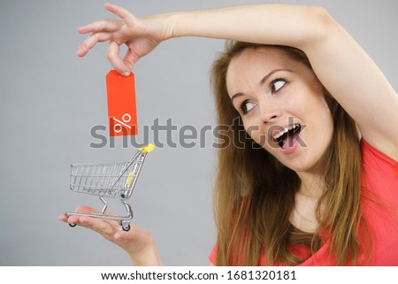 Happy woman enjoying affordable sales. Female holding small shopping trolley cart with percentage sale sign, on grey