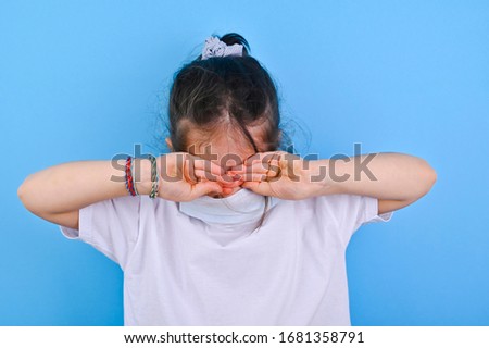 Baby in coronavirus. World pandemic concept COVID 19. Little girl in a protective medical mask closes her eyes with her hands. Emotion baby ea photo. Copy space and blu background 
