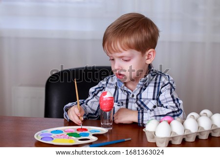 Little boy paints eggs with colored paints
