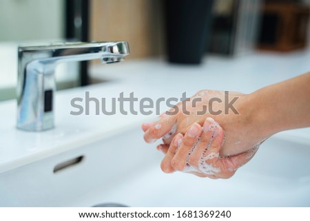 Woman washing hands with water and soap in bathroom sink. Hands woman opening silver faucet or water tap with white washing sink in public toilet.