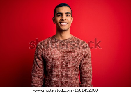 Young handsome african american man wearing casual sweater standing over red background with a happy and cool smile on face. Lucky person.