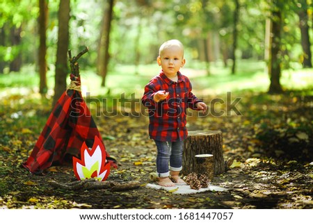 little child in a plaid shirt in the forest with a tent. Children's photo shoot. Little boy having fun playing outdoors on a summer day.