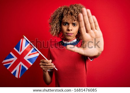 Young african american curly woman holding uk flag celebrating brexit referendum with open hand doing stop sign with serious and confident expression, defense gesture