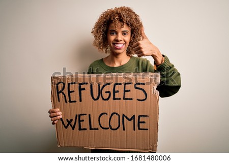 African american woman asking for immigration holding banner with wlecome refugees message happy with big smile doing ok sign, thumb up with fingers, excellent sign