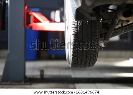 Close-up view of automobile wheel hanging over ground on mechanical lift. Car service center and auto maintenance concept. Professional equipment in garage