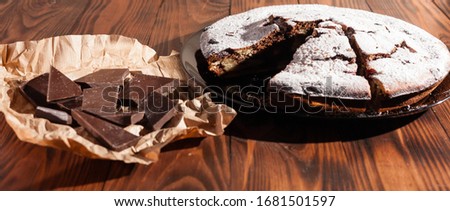 Rustic chocolate cake sprinkled with icing sugar. Chocolate cake on a wooden table.