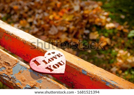 Red wooden heart on the wooden bench background in autumn