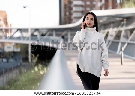 Stock photo of a young business woman having a conversation on the phone. She is serious. She is walking on the street. She is wearing casual clothing.