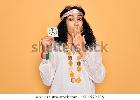 African american curly hippie woman wearing sunglasses holding reminder with peace symbol cover mouth with hand shocked with shame for mistake, expression of fear, scared in silence, secret concept