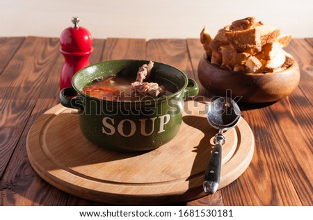 Rustic meat bone soup / broth sprinkled with green onions on a wooden table with crackers.