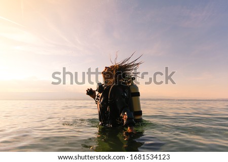 Female Scuba Dive Instructor Wearing a Dry Suit, a Twin Tank and Holding Fins Flipping Wet Hair in the Air Royalty-Free Stock Photo #1681534123