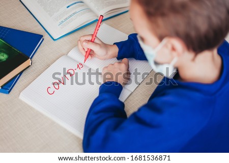 Distance learning online education. A schoolboy sits at a table and writes in a notebook, nearby are textbooks. View from above. The inscription "Covid-19" in red. Royalty-Free Stock Photo #1681536871