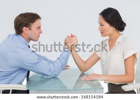 Side view of serious young business couple arm wrestling at office desk