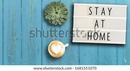 lightbox with appeal text STAY AT HOME on rustic wooden table with potted plant and coffee, social distancing concept during coronavirus pandemic