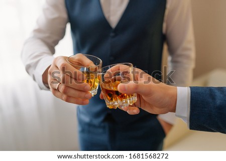 The groom and groomsman drinking a whiskey, celebrating wedding day. Hands of man holding glasses with alcohol and toasting. group of men cheering and clinking with drinks at wedding reception Royalty-Free Stock Photo #1681568272