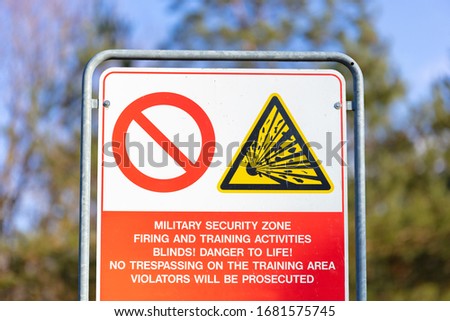 A warning sign on the edge of a military training area in Germany. Entering the site is dangerous. There is a risk of injury from explosions. In the background is a forest.