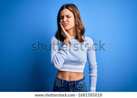 Young beautiful blonde girl wearing casual sweater standing over blue isolated background touching mouth with hand with painful expression because of toothache or dental illness on teeth. Dentist