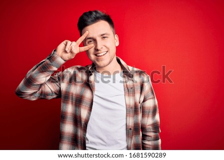 Young handsome caucasian man wearing casual modern shirt over red isolated background Doing peace symbol with fingers over face, smiling cheerful showing victory