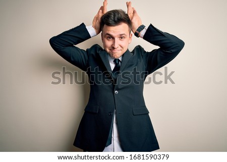 Young handsome business man wearing elegant suit and tie over isolated background Doing bunny ears gesture with hands palms looking cynical and skeptical. Easter rabbit concept.