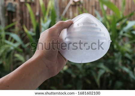 hand holds a white medical face mask on a Blurred background, green  Blurred background