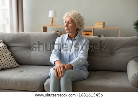 Pensive mature woman sit on sofa in living room look in distance window thinking of lonely life, thoughtful elderly female rest on couch at home feel melancholic, miss old days, solitude concept Royalty-Free Stock Photo #1681615456