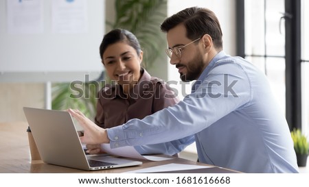 Smiling diverse businesspeople sit at desk work on laptop together discussing project or idea, happy multiracial colleagues cooperate using computer gadget, brainstorm at office meeting Royalty-Free Stock Photo #1681616668