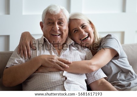 Happy older wife and husband hugging and laughing together, having fun, smiling mature father and adult middle-aged daughter sitting on cozy sofa at home, old couple enjoying tender moment Royalty-Free Stock Photo #1681617193