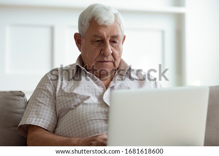 Serious older man using laptop close up, looking at screen, watching video or surfing internet, focused mature male using online clinic service or searching insurance information, medical app