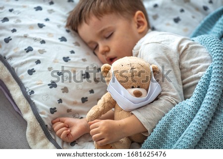 Little boy sleeping in bed with medical mask embracing his teddy bear. Home isolation coronavirus covid-2019 quarantine. Children and illness disease concept