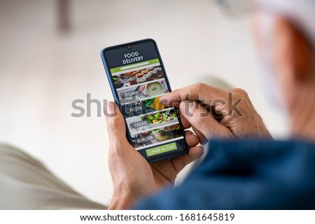 Top view of man hands holding smartphone while order food delivery at home. Back view of mature man using food delivery app with mobile phone to order lunch.  Royalty-Free Stock Photo #1681645819