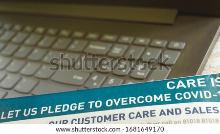 Part of Newspaper showing pledge to overcome Corina virus epidemic COVID - 19. Laptop keyboard out of focus Background.