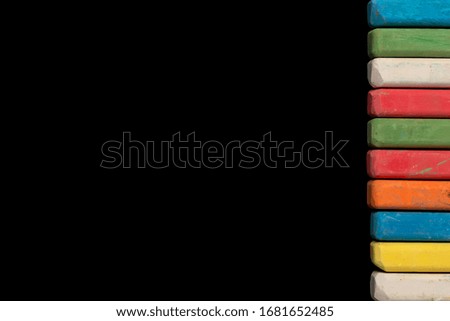 colored children's crayons on a black background on the right side lined in a row, top view. free space for pictures and text