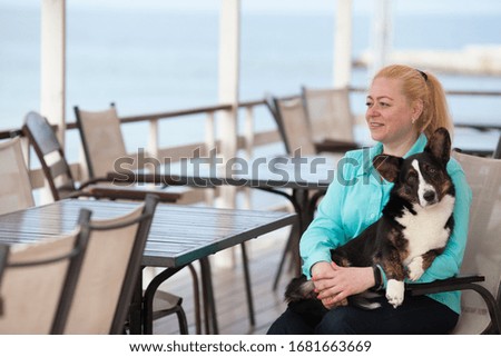 An adult woman is sitting in a cafe holding her dog Welsh Corgi cardigan. copyspace. The concept of a warm relationship between the owner and the pet.