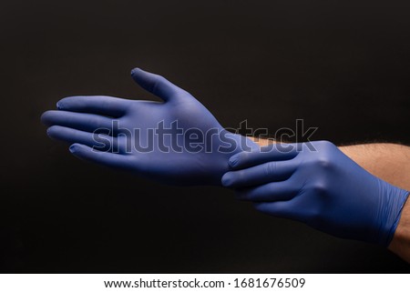 Male brown skin doctor hands put blue nitrile gloves on. Close up on a black background. CPR First AID hands in Gloves Safety Rule.  Royalty-Free Stock Photo #1681676509