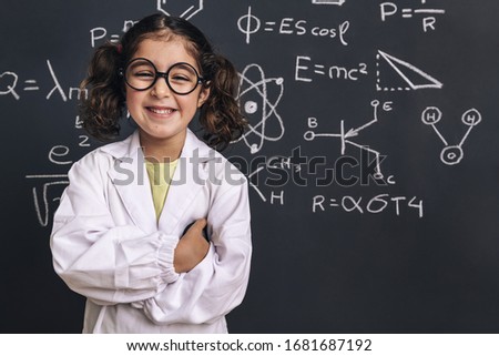 smiling little girl science student with glasses in lab coat on school blackboard background with hand drawings science formula pattern, back to school and successful female career concept Royalty-Free Stock Photo #1681687192