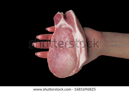 Raw pork steak, a large piece, in a female hand close-up, black backdrop.