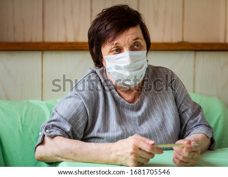 an adult woman, a pensioner, in a medical mask , holding a dysenfector, sitting at home in quarantine because of the COVID-19 pandemic
