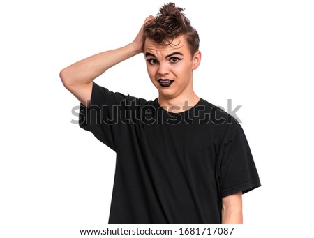 Unhappy teen boy student in style of punk goth dressed in black t-shirt, isolated on white background. Upset Teenager Back to school. Sad or thoughtful child with spooking makeup looks at camera.