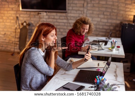 Young people on a break in a modern office; freelacers working in coworking space, woman having a video call using smart phone