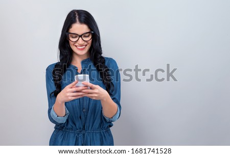 Young woman using her cellphone on a gray background
