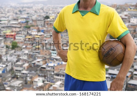 Brazilian football player stands in Brazil team colors holding vintage soccer ball in front of favela background in Rio de Janeiro